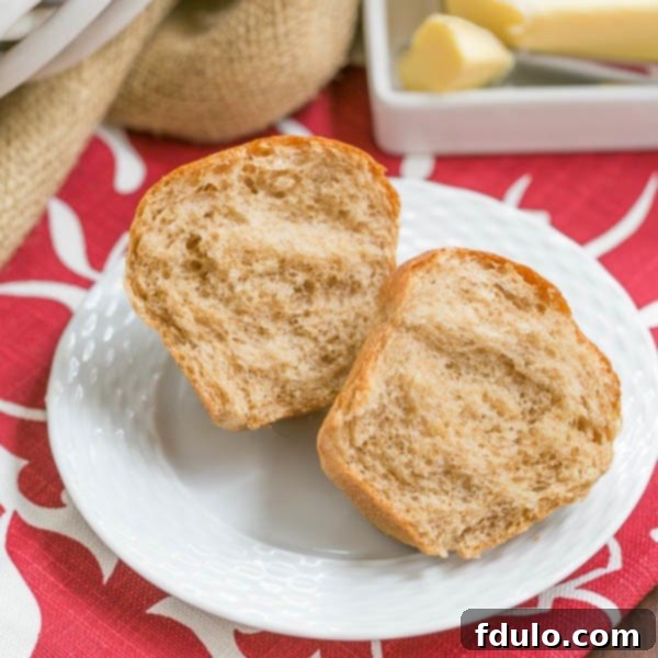A close-up shot of golden-brown Whole Wheat Dinner Rolls, perfectly baked and glistening, perhaps with a slight butter sheen, stacked in a rustic ceramic basket.