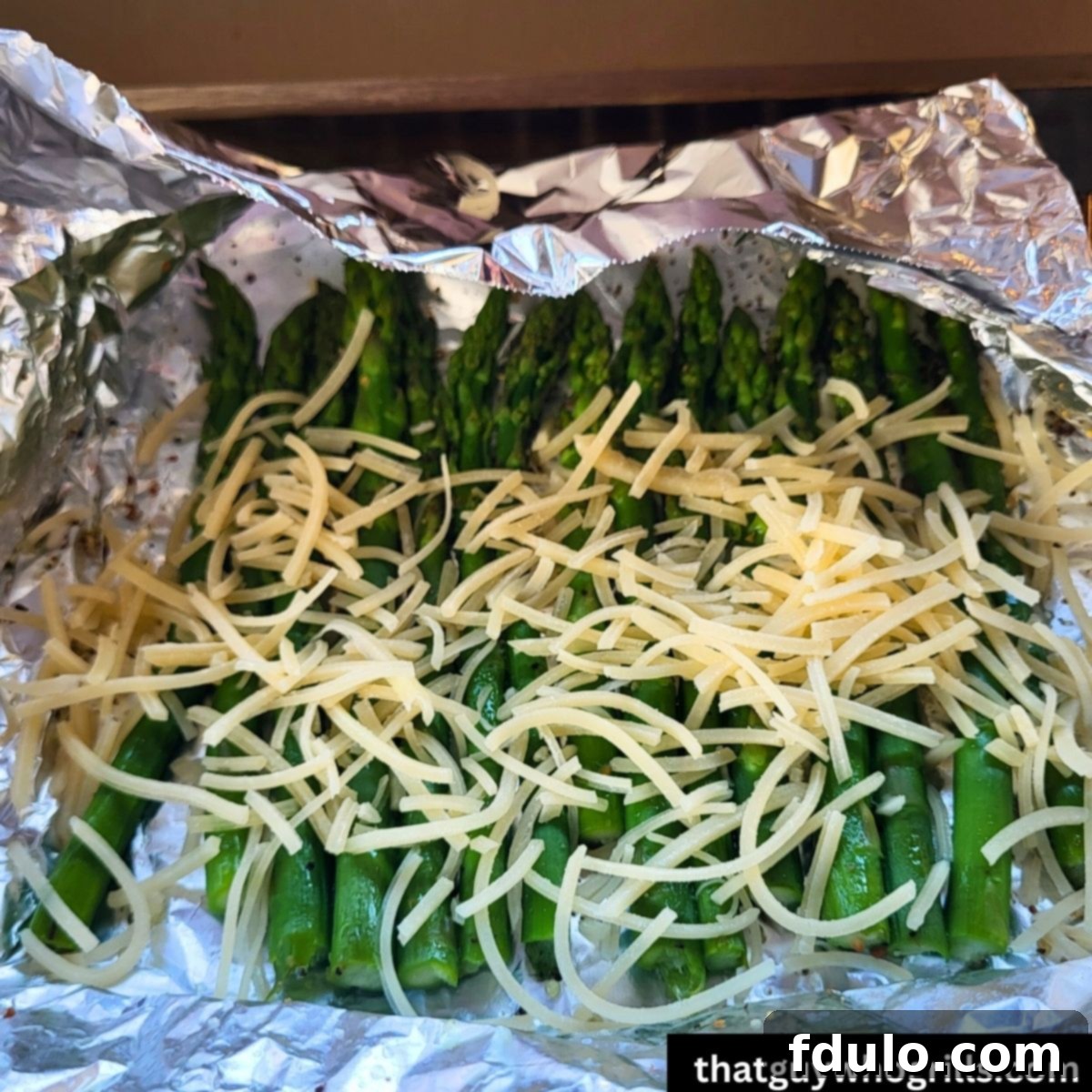 Parmesan cheese sprinkled on grilled Asparagus in tin foil packet before melting