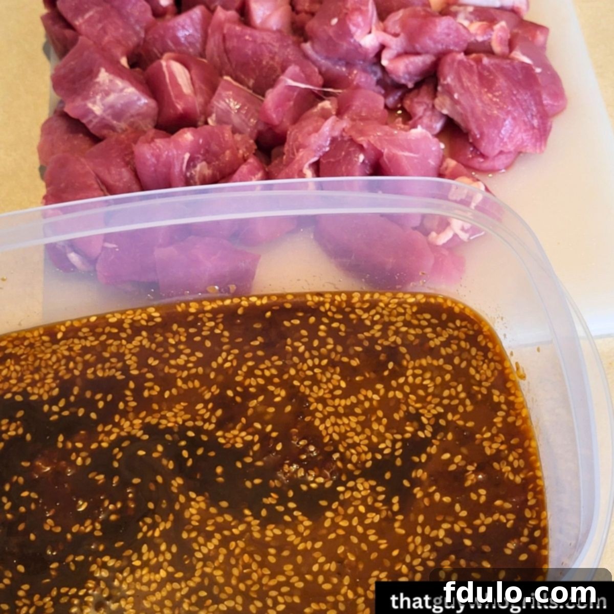 Diced pork tenderloin resting beside a container of vibrant Teriyaki Pork marinade, ready to absorb flavor.
