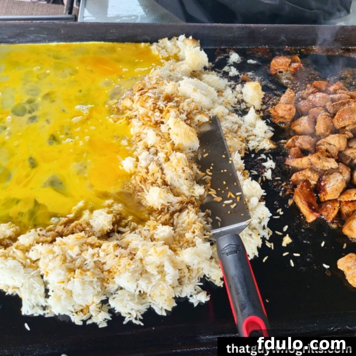 The Blackstone Griddle alive with the sizzling action of Teriyaki Pork Fried Rice cooking to perfection, components neatly separated.
