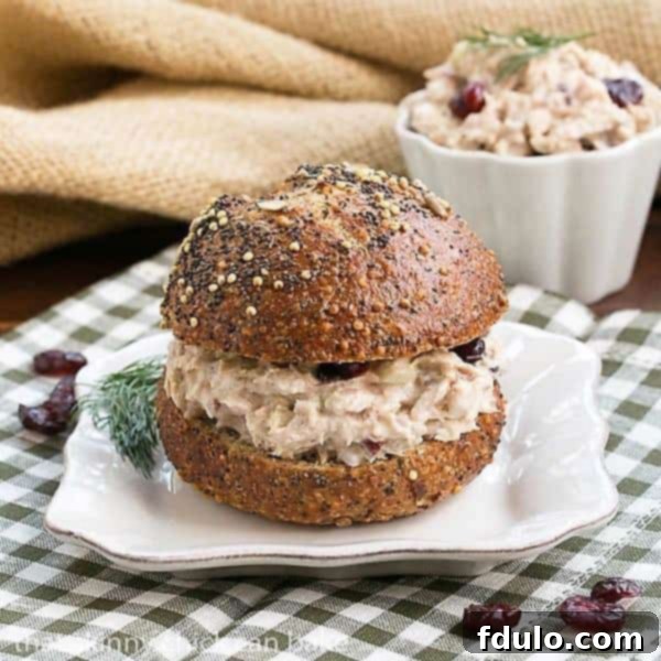 A gourmet tuna salad sandwich on a seedy bun, served on a square white plate, ready to be enjoyed as a quick and flavorful meal.