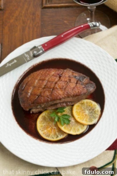 Perfectly seared duck breasts with rich red wine sauce, served on a white plate with a red-handled knife.