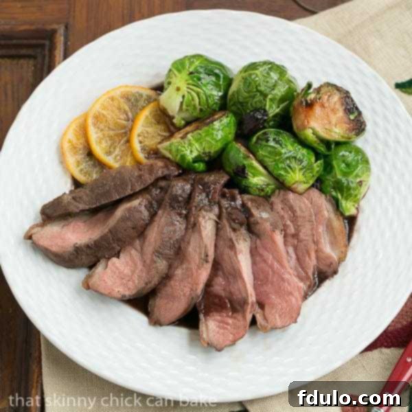 Pan-Seared Duck Breasts with orange slices and Brussels sprouts on a festive plate.