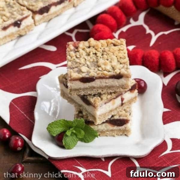 Stacked Cranberry Cheesecake Bars on a white dessert plate, showcasing the distinct layers of crust, cream cheese, and cranberry with a streusel topping.