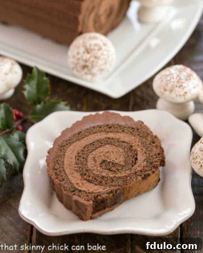 A perfectly sliced Bûche de Noël (Yule Log Cake) revealing its rich chocolate mousse filling and ganache frosting, presented on a square plate, ready to be enjoyed as a festive French Christmas dessert.