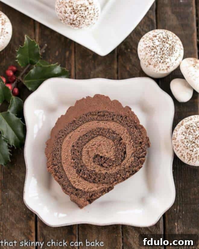 An overhead view of a beautifully decorated slice of Christmas Yule Log Cake Roll, garnished with whimsical meringue mushrooms, showcasing the intricate detail and festive spirit of this traditional French dessert.