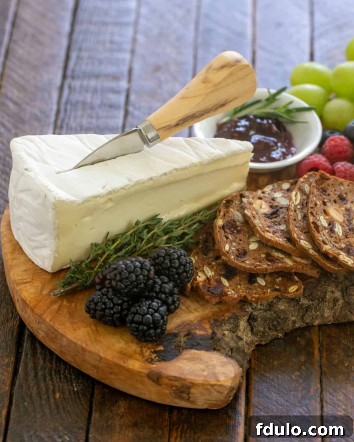 Brie with crackers and fruit on a beautiful wooden cheese board.