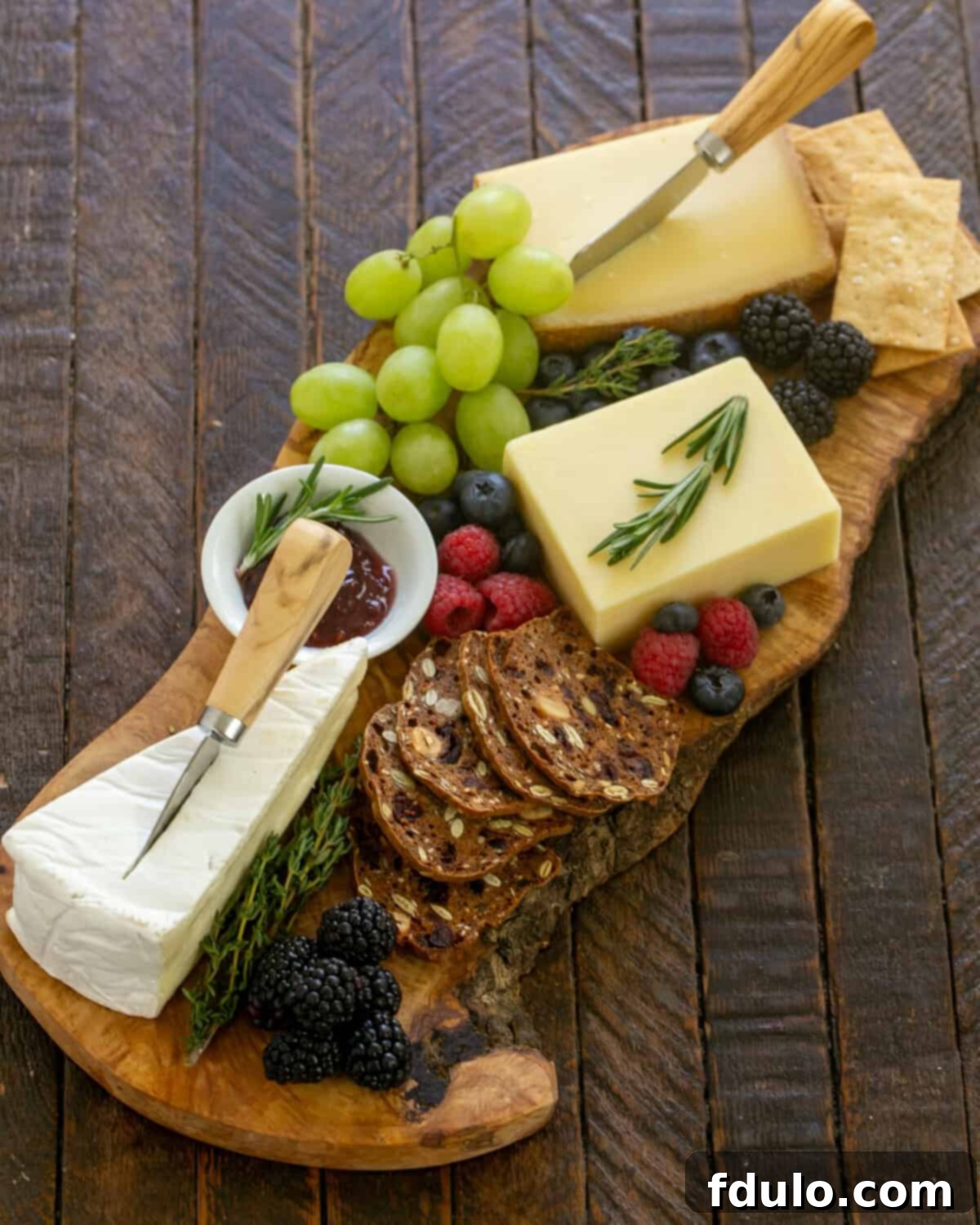 overhead view of wooden cheeseboard topped with fruit, cheese, and crackers.