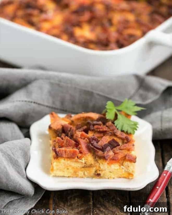 A perfectly baked slice of Easy Bacon and Egg Strata on a white plate, with the full casserole dish blurred in the background, showcasing golden croutons, melted cheese, and savory bacon.