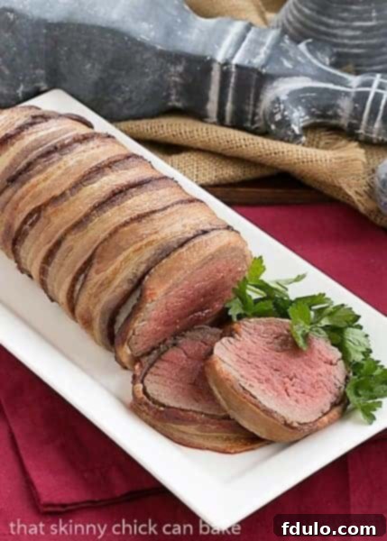 A pristine white platter showcasing a whole bacon-wrapped beef tenderloin, exquisitely roasted and ready for slicing, alongside a bowl of creamy Gorgonzola sauce.