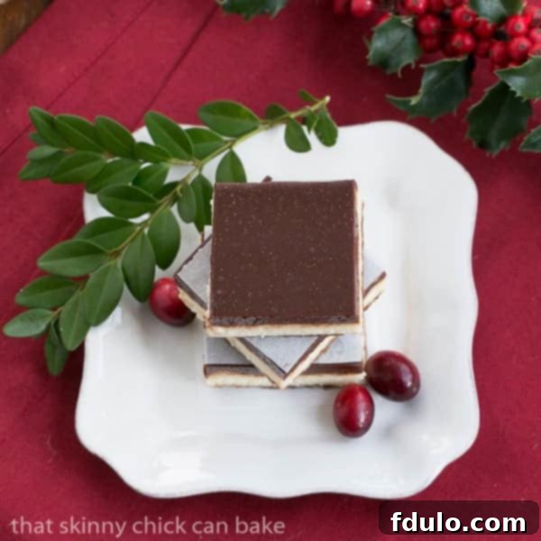 Elegant Ganache Topped Cheesecake Bars, beautifully arranged on a white plate, garnished with festive cranberries and boxwood for a touch of sophistication.
