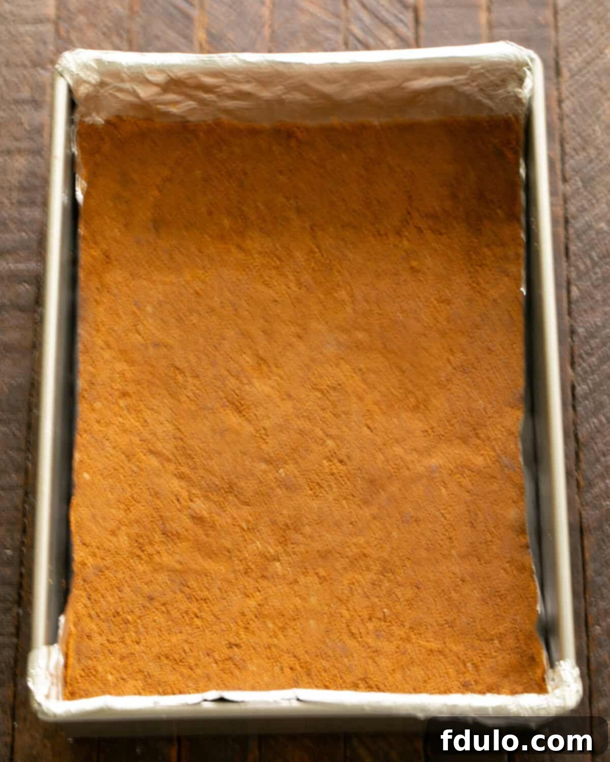 Firmly patting the Biscoff cookie crumb mixture onto the bottom of a baking pan.