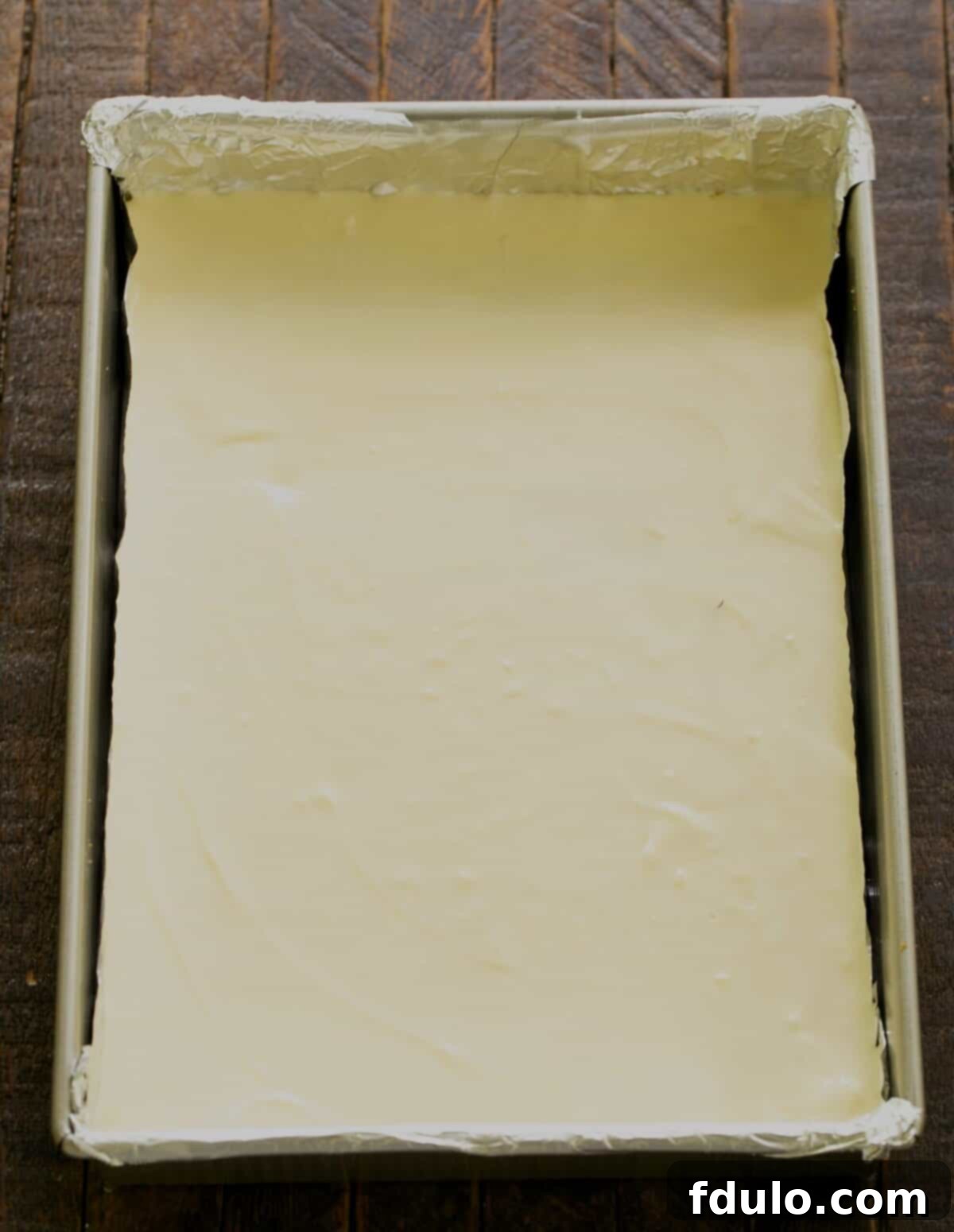 Spreading smooth cheesecake batter evenly over the Biscoff crust in the baking pan.