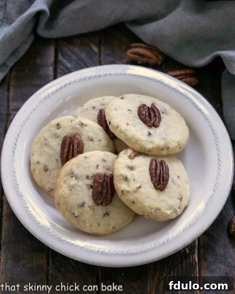 Four golden-brown Pecan Sandies cookies neatly arranged on a round white plate, beautifully presented and ready for tasting.