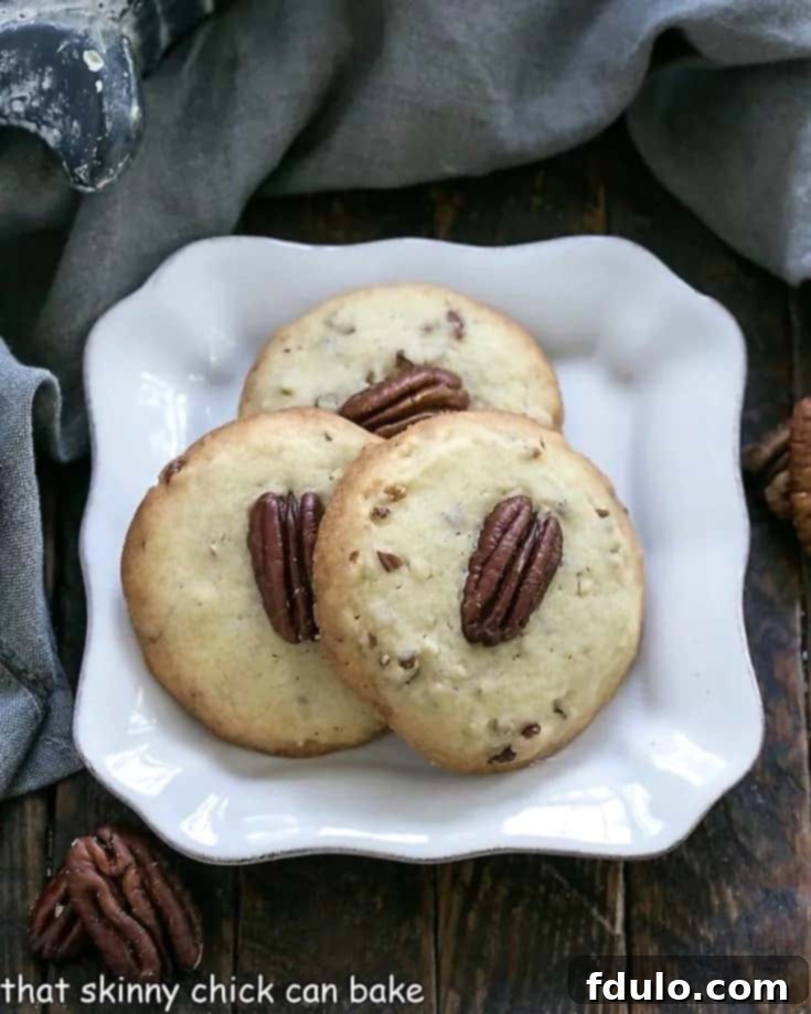 Overhead view of three perfectly baked Pecan Sandies on a square white decorative plate, garnished with a few whole pecans, highlighting their crumbly texture.