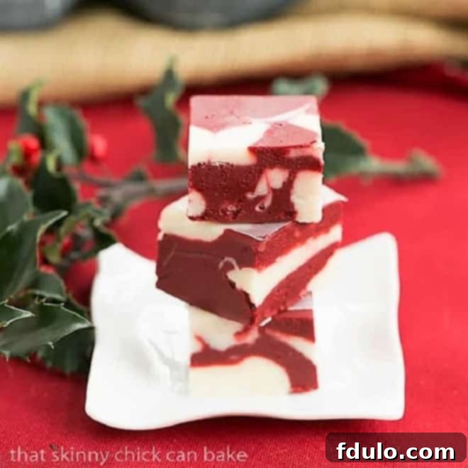 Close-up shot of a square of marbleized Red Velvet Fudge on a small, rippled white plate, showcasing the vibrant red and white swirls.