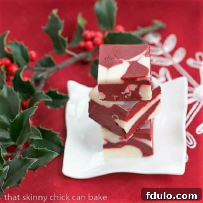 A beautiful stack of three squares of Red Velvet Fudge on a small white plate, garnished with a sprig of fresh holly berries for a festive touch.