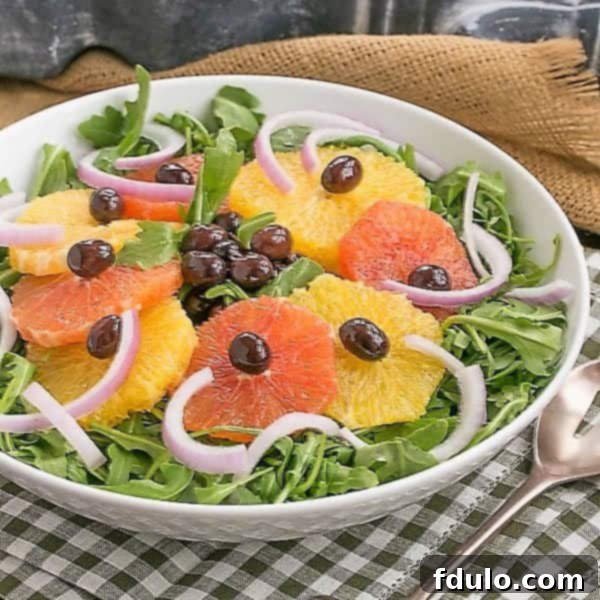 A vibrant Orange Olive Salad featuring citrus segments and dark olives, served on a bed of fresh arugula in a pristine white bowl.