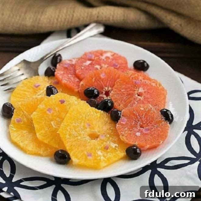 A close-up shot of Moroccan Orange Salad ingredients on a white plate, showcasing vibrant orange slices, dark Nicoise olives, and thinly sliced red onion.