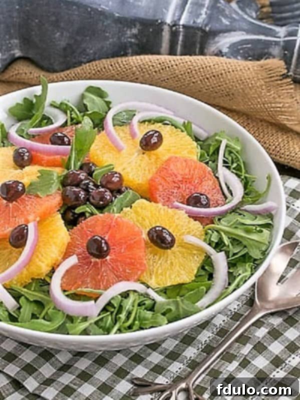 A beautifully presented Moroccan Orange Salad with Nicoise olives on a bed of fresh arugula, served in a white bowl on a charming checked napkin.
