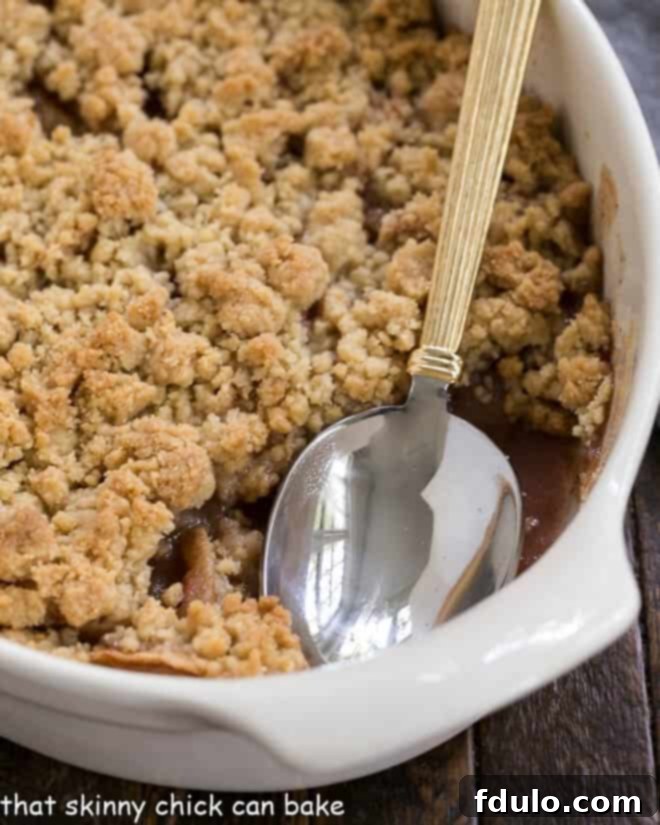 Easy Apple Crisp in a white ceramic baking dish with a serving spoon, showcasing the golden topping.