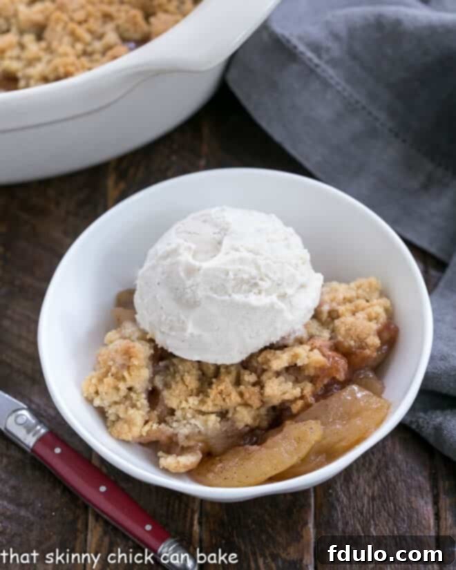 Serving of Easy Apple Crisp in a small white bowl with a scoop of vanilla ice cream melting on top.