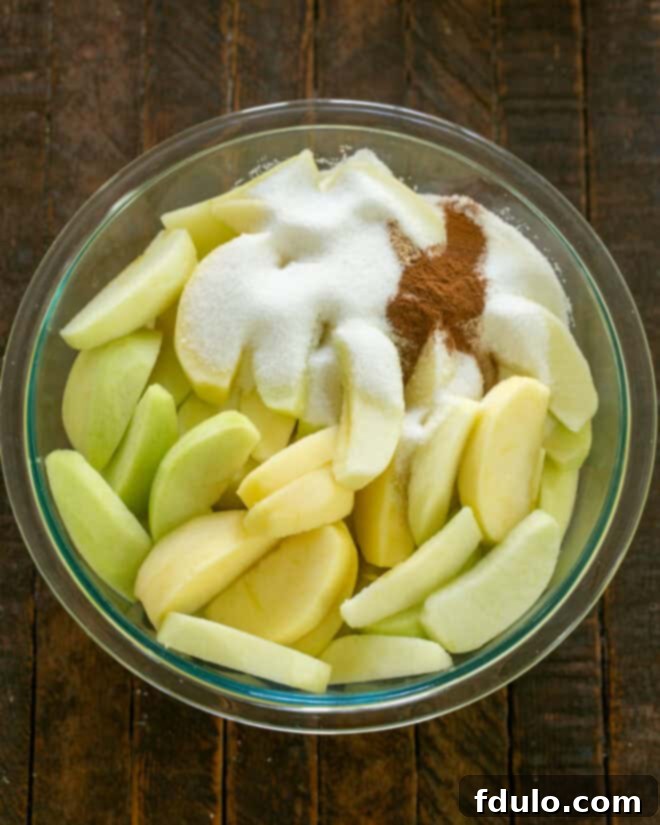 Sugar and ground spices like cinnamon and nutmeg added to sliced apples in a bowl.