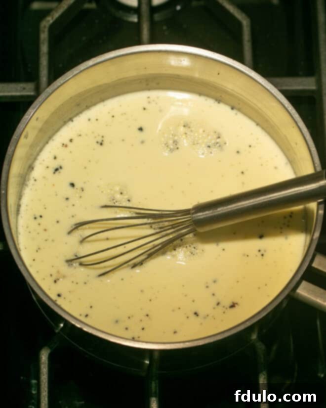 Heavenly Crème Brûlée Perfection 6 Tempered egg yolks slowly being added back to the hot cream mixture in the pan, whisking constantly.