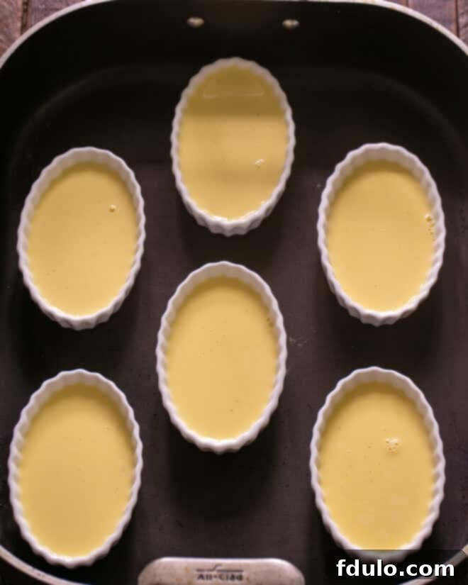 Heavenly Crème Brûlée Perfection 8 Ramekins filled with custard placed in a larger roasting pan, with boiling water being poured to create a water bath.