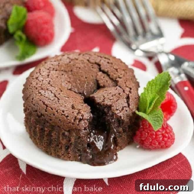 Chocolate Lava Cakes broken open on a white plate with raspberries and mint