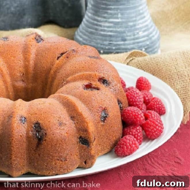 Raspberry Amaretto Bundt Cake on a cake plate with fresh raspberries.
