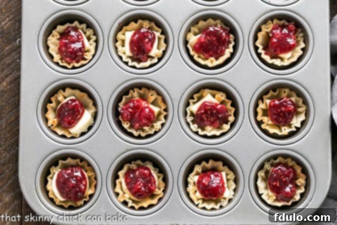Unbaked Raspberry Brie Bites nestled in a mini muffin tin, ready for the oven, with a rustic kitchen towel in the background.