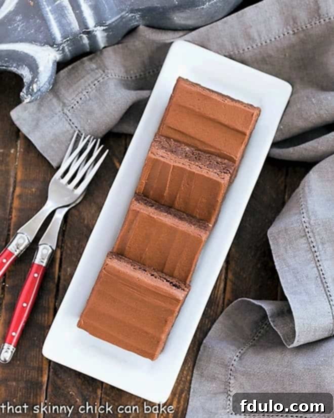 Overhead view of perfectly cut and frosted fudgy brownies lined up neatly on a narrow white serving tray.