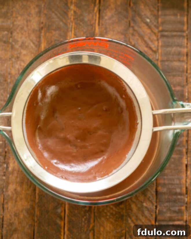 Straining the cooked chocolate pudding through a fine-mesh sieve.