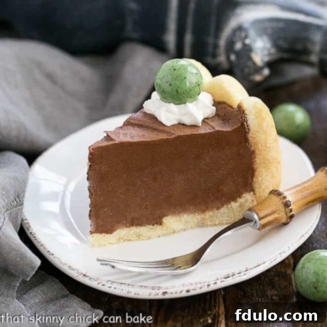 A perfectly sliced piece of Irish Chocolate Mousse Cake on a white ceramic plate, adorned with a dollop of whipped cream and a festive green candy.