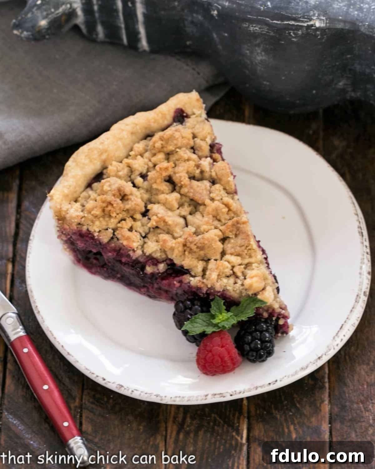 Overhead view of a slice of mixed berry pie on a white plate with fresh berry garnish.