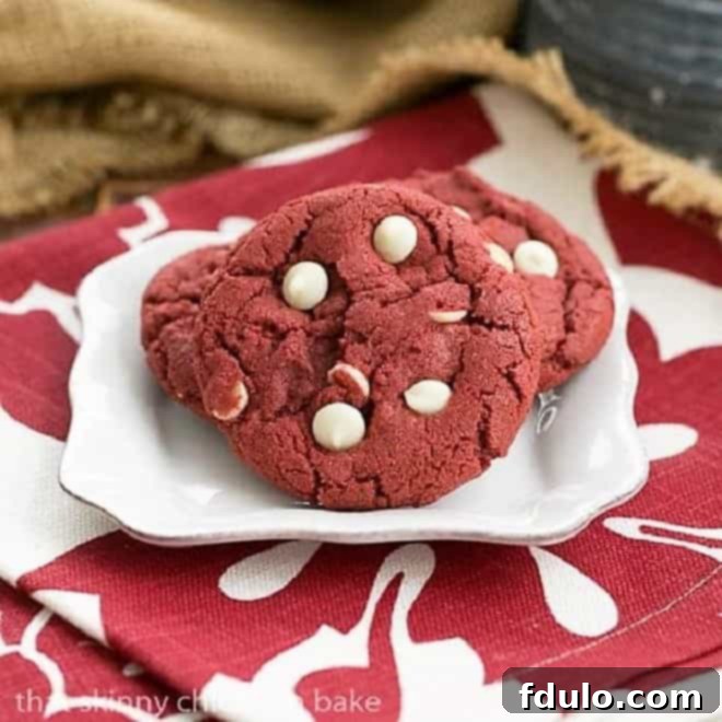 Freshly baked Red Velvet Cookies with White Chocolate Chips on a square white plate, artfully arranged on a festive red and white striped napkin. The cookies are soft, chewy, and speckled with melting white chocolate.