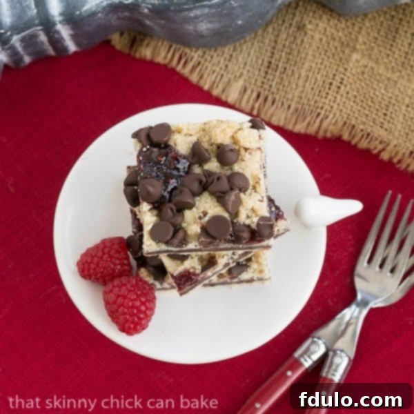 An overhead view of freshly baked Chocolate Raspberry Crumb Bars presented on a white pedestal, set against a vibrant red napkin.