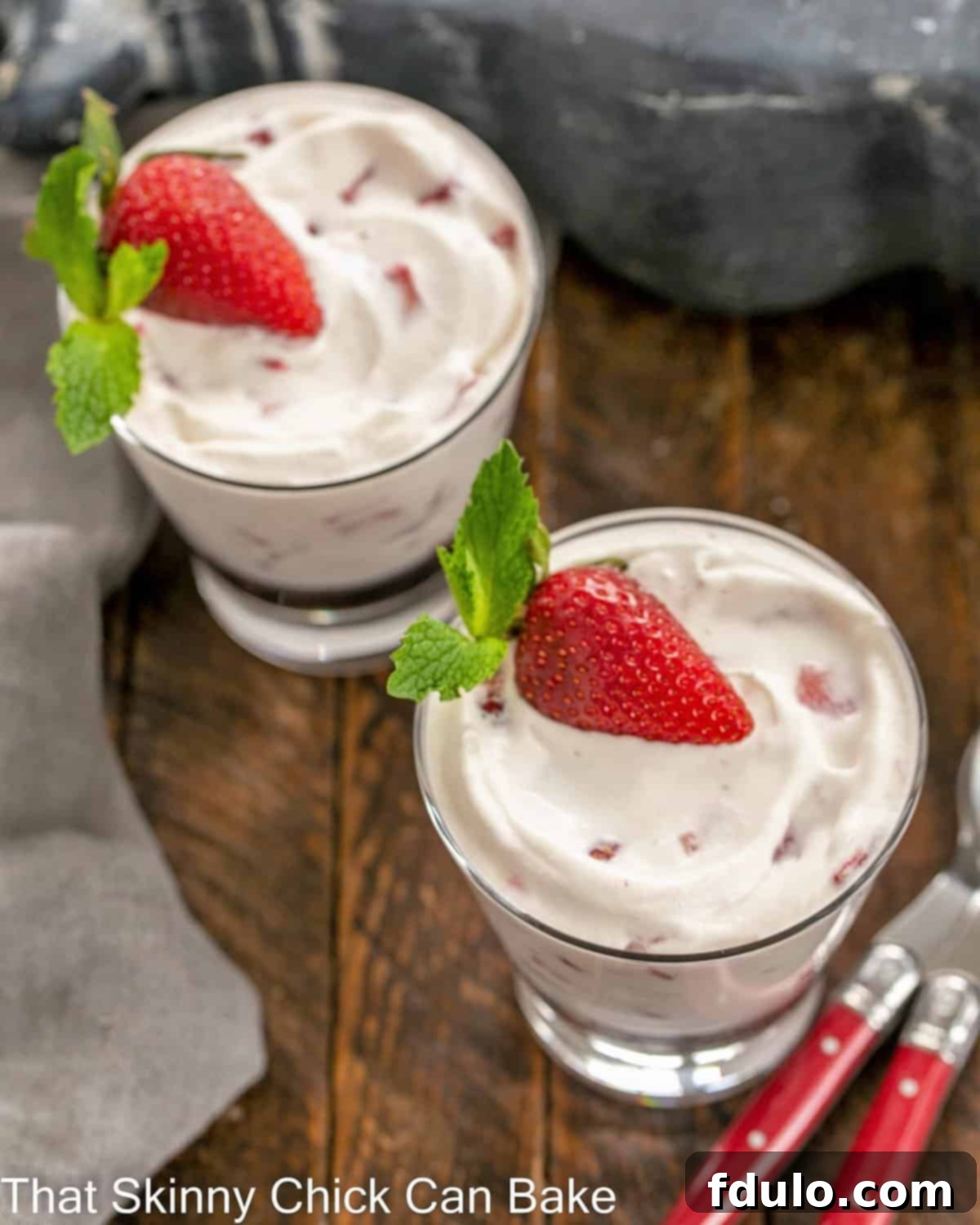 Overhead view of two luscious No-Bake Strawberry Fools served in clear glass dishes, accompanied by two red-handled spoons, highlighting their inviting texture and vibrant color.