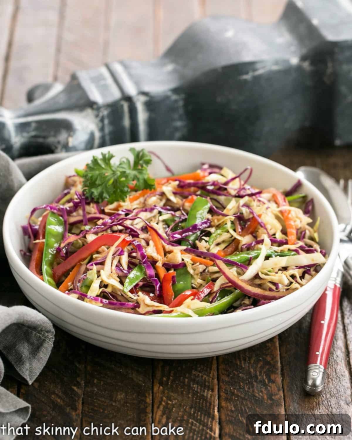 Asian Coleslaw in a white serving bowl, garnished with sesame seeds and fresh herbs.