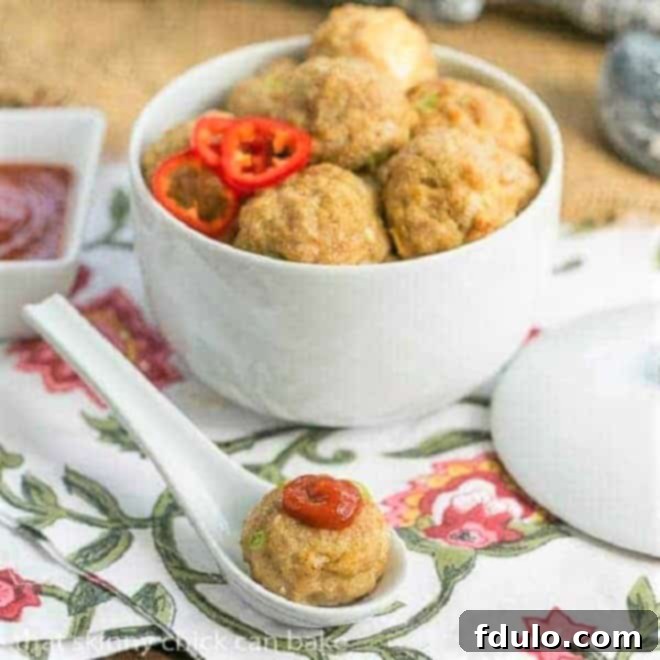 Sesame Ginger Chicken Meatballs in a white ceramic bowl, with one meatball topped with Sriracha in a ceramic spoon, ready to be served as an appetizer.