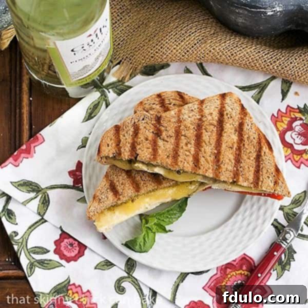 Top-Down View of a Delicious Chicken Pesto Grilled Cheese Sandwich Aerial view of a Chicken Pesto Grilled Cheese sandwich, garnished with fresh basil, served on a white plate with a red-handled fork.