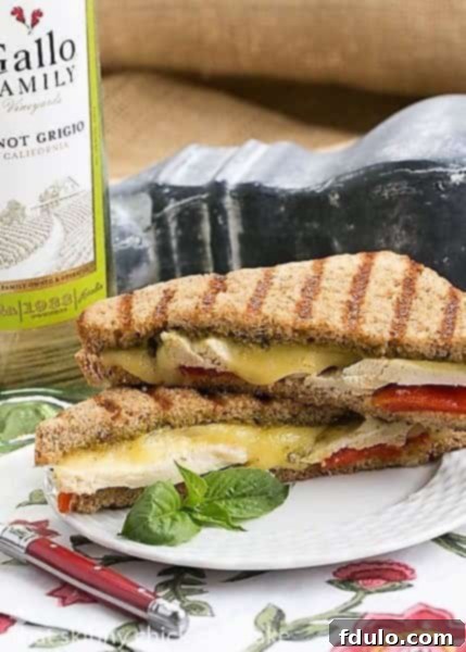 Artisanal Chicken Pesto Grilled Cheese - Perfect for Any Meal Close-up of a golden-brown Chicken Pesto Grilled Cheese on a white plate, resting on a floral napkin, highlighting its delicious texture.