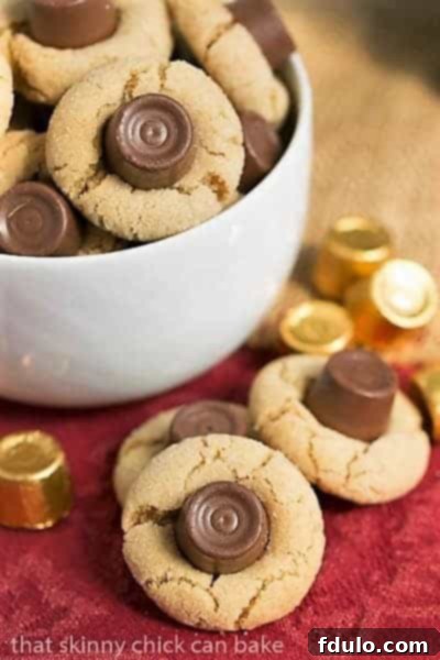 A white bowl brimming with Rolo Peanut Blossoms, with additional cookies and candies casually scattered on the side.