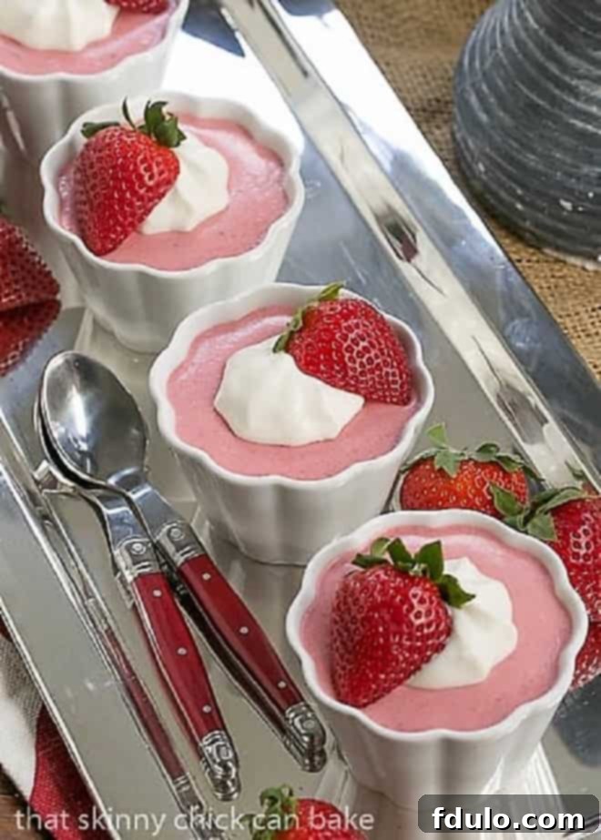 Strawberry Mousse in 4 white ramekins lined up on a silver tray with red handled spoons.