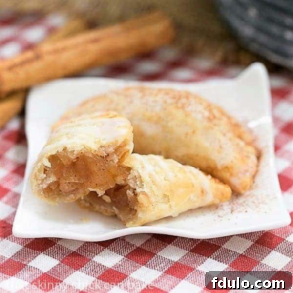Two freshly made Fried Apple Pies on a ceramic plate, one carefully broken open to reveal the steam and cinnamon-spiced apple filling