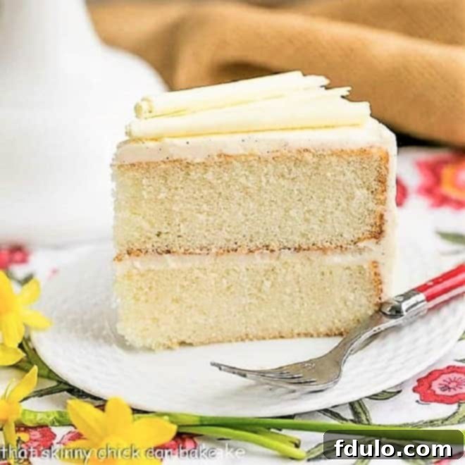 A perfectly sliced piece of white birthday cake, showcasing its tight, moist crumb, resting on a pristine white plate beside a elegant red-handled fork.