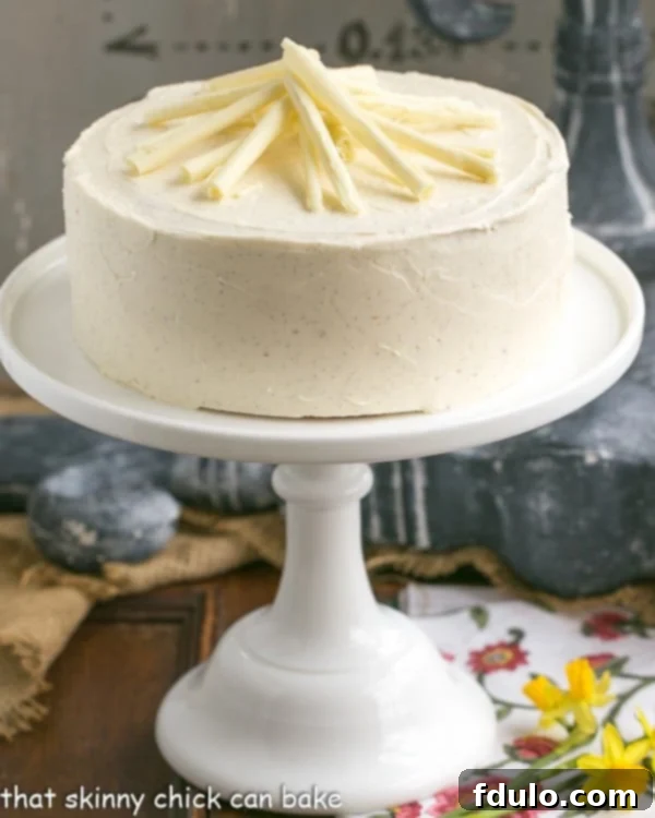 An elegantly decorated white birthday cake, topped with delicate white chocolate curls, presented on a classic cake stand, ready for celebration.