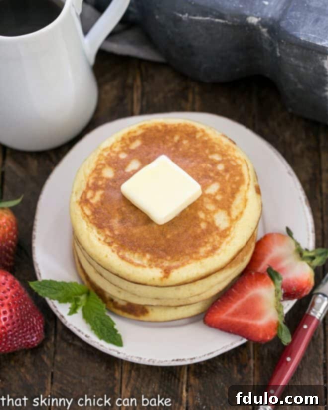 A stack of golden brown buttermilk pancakes, generously topped with a melting pat of butter and garnished with a medley of fresh sliced berries, glistening with syrup.