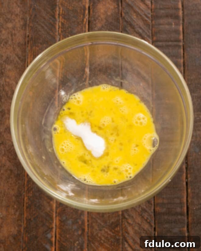 A whisked egg in a bowl, with salt and sugar granules ready to be incorporated.